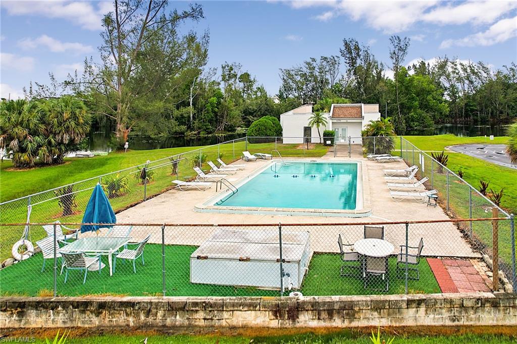 Fenced swimming pool area featuring a paved deck, an adjacent lawn, and a nearby building with a tiled roof