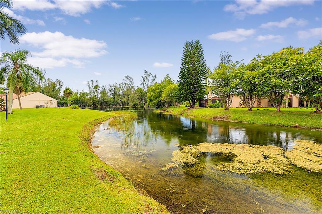 Waterfront property featuring a lush green lawn, mature trees, and a beige exterior structure