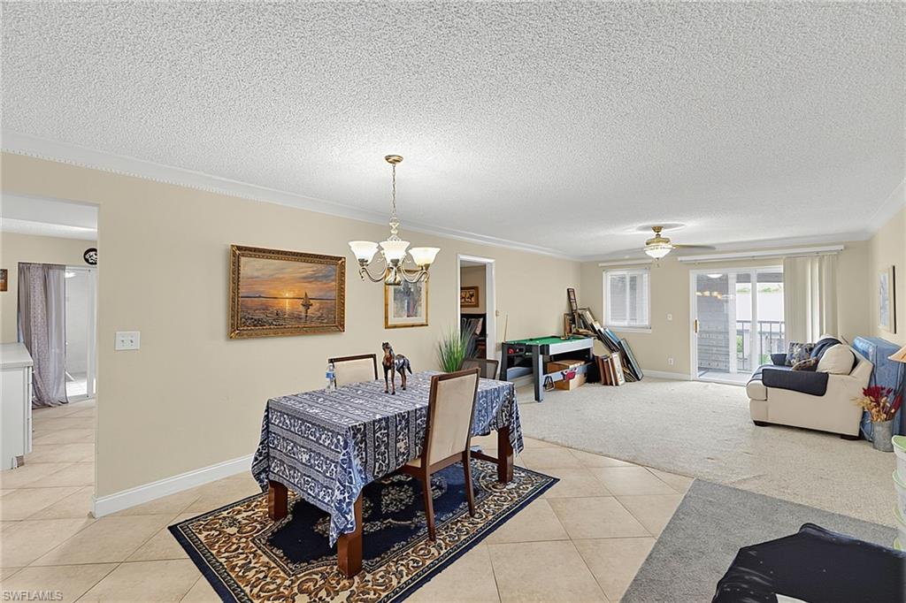 Dining area with crown molding, chandelier, tile flooring, and a large opening to a carpeted living space featuring a ceiling fan and sliding glass doors to an exterior balcony