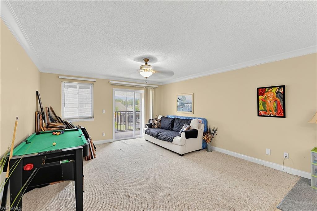 Carpeted room featuring crown molding, a ceiling fan with light fixture, and a sliding glass door providing access to an outdoor area with a black railing