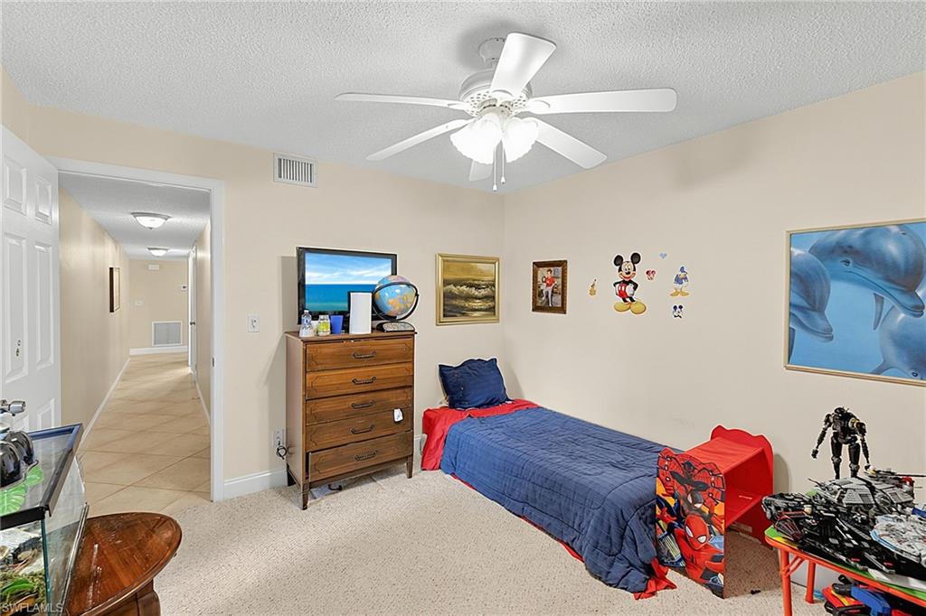 Carpeted room featuring a ceiling fan, light-toned walls, and a doorway opening to a tiled hallway