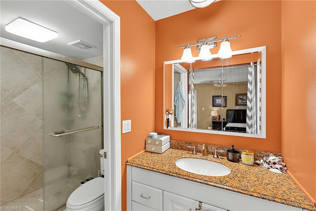 Bathroom featuring a granite countertop vanity with an undermount sink, brushed brass faucet, and white cabinetry