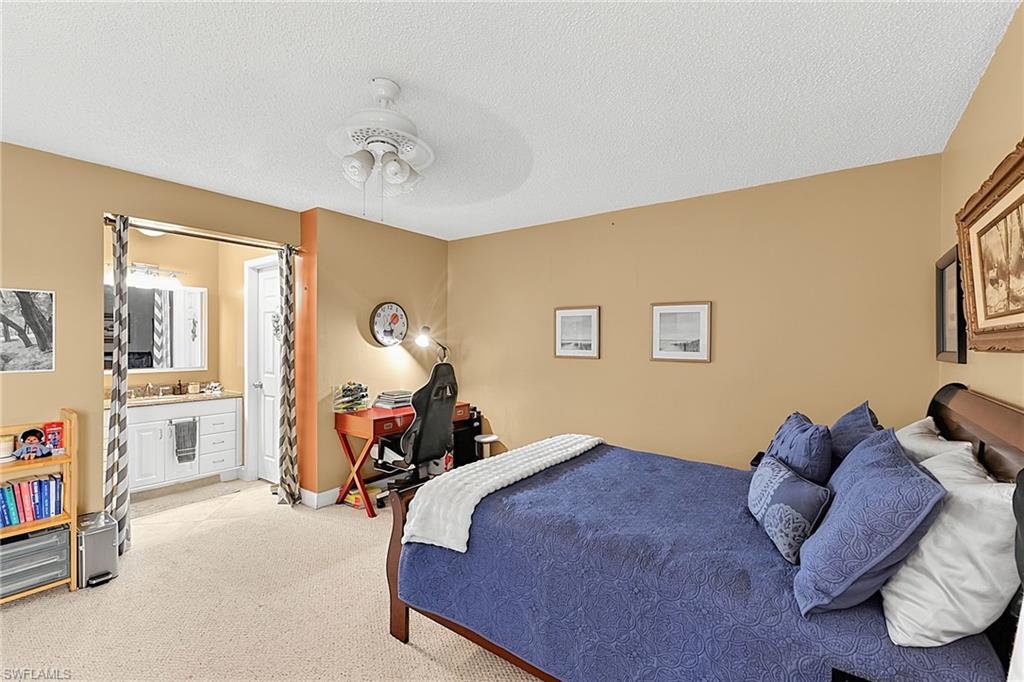 Carpeted bedroom featuring a ceiling fan with light fixture and a built-in vanity with a sink and storage cabinetry visible through an open doorway