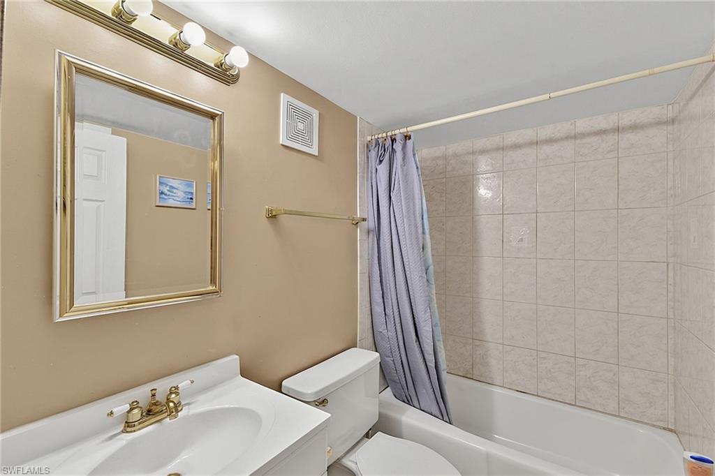 Full bathroom featuring a white vanity with integrated sink, brass-finish faucet, and a wall-mounted mirror