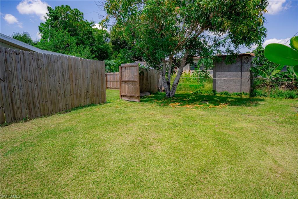 Expansive grassy yard area featuring a wood privacy fence and mature trees