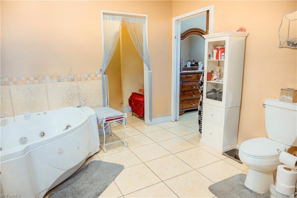 White corner soaking tub, light-colored tile flooring, and a white toilet