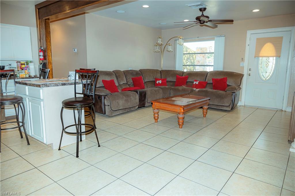 Tile flooring, decorative glass entry door, ceiling fan with light fixture, window with horizontal blinds, built-in breakfast bar with white cabinetry