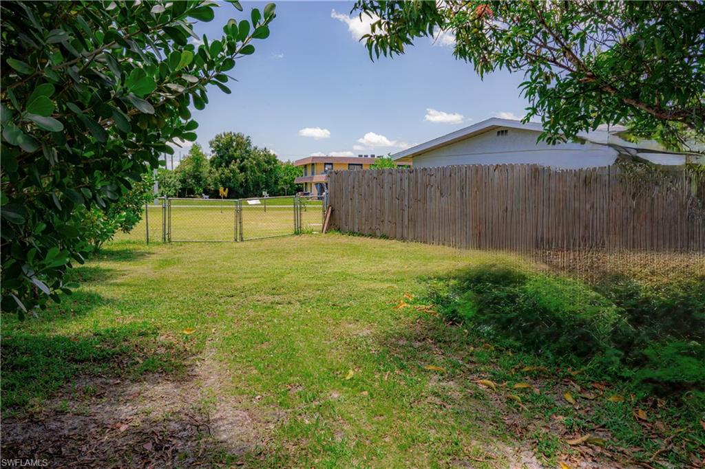 Expansive grassy area featuring a wooden privacy fence, chain link fencing, and mature trees