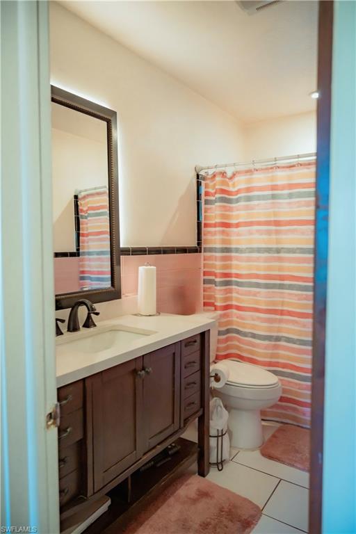 White tile flooring, wood-finish vanity with countertop sink, dark bronze faucet, and framed mirror with backlighting