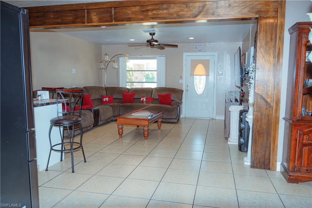 Tile flooring, wood-finish beam accents, ceiling fan, and front door with decorative glass inlay