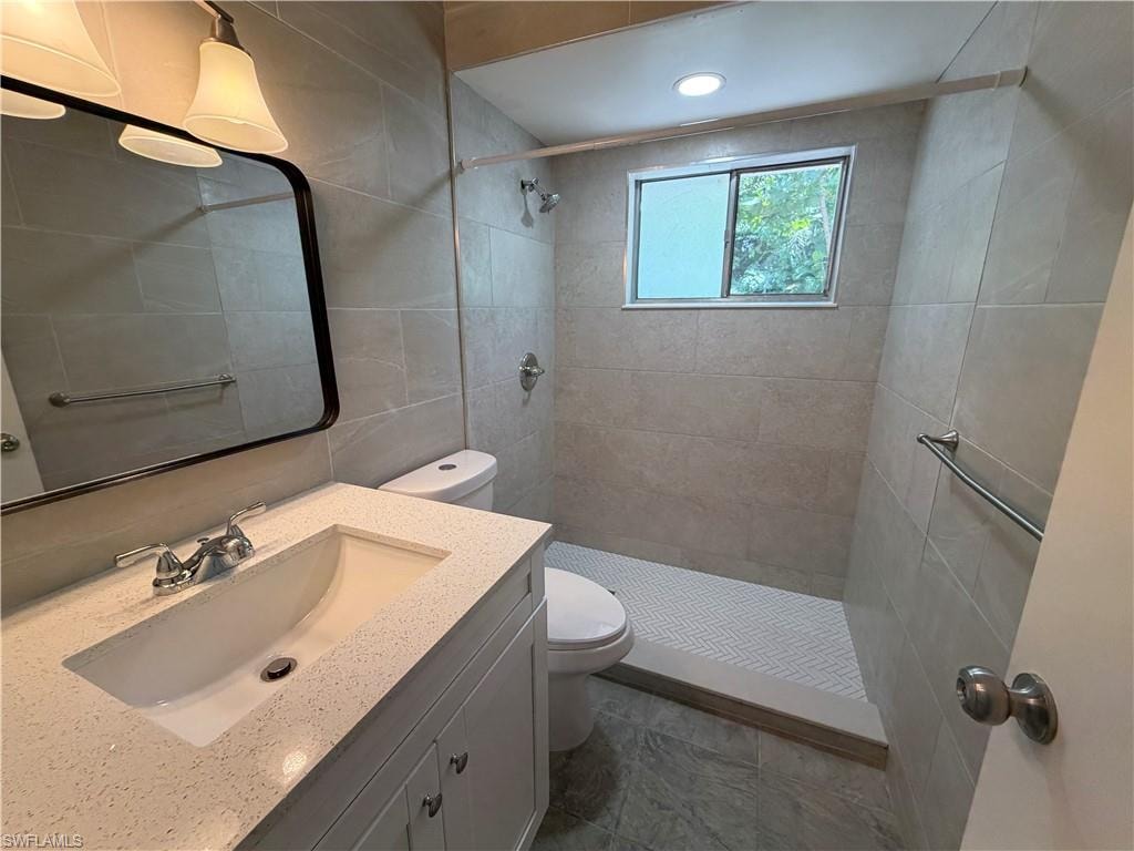 Vanity with integrated sink and quartz-finish countertop, contemporary wall mirror with black trim, tiled shower with herringbone pattern floor, recessed lighting