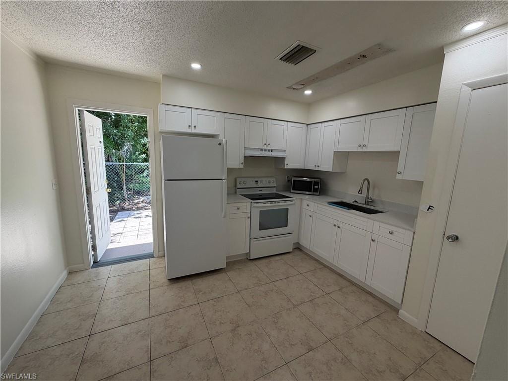 Kitchen featuring white cabinetry, light-toned countertops, tile flooring, and a white appliance suite