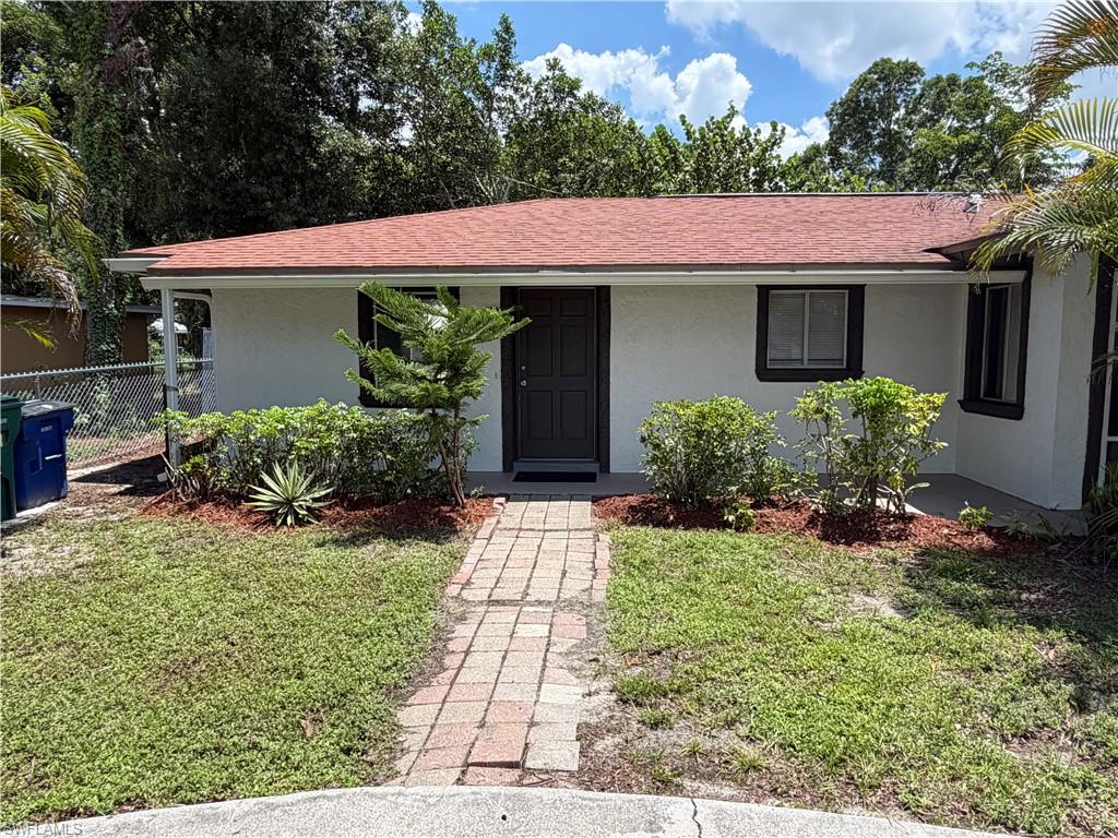 White exterior finish with a red shingle roof, dark trim windows, and a brick paver walkway leading to the entrance