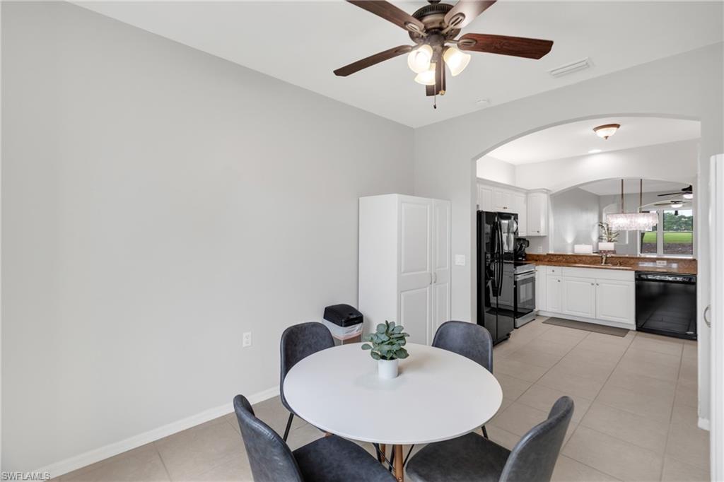 Arched doorway entry to the kitchen featuring white cabinetry, black appliances, and a ceiling fan with integrated lighting