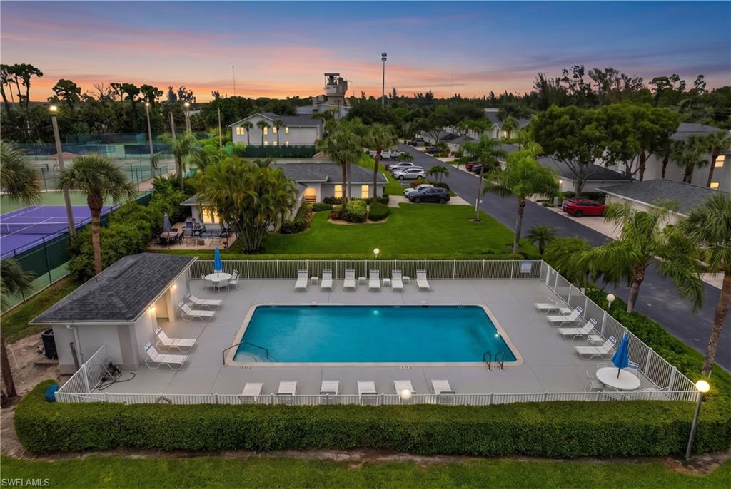 Community swimming pool with surrounding lounge seating, adjacent pool house, and nearby tennis courts