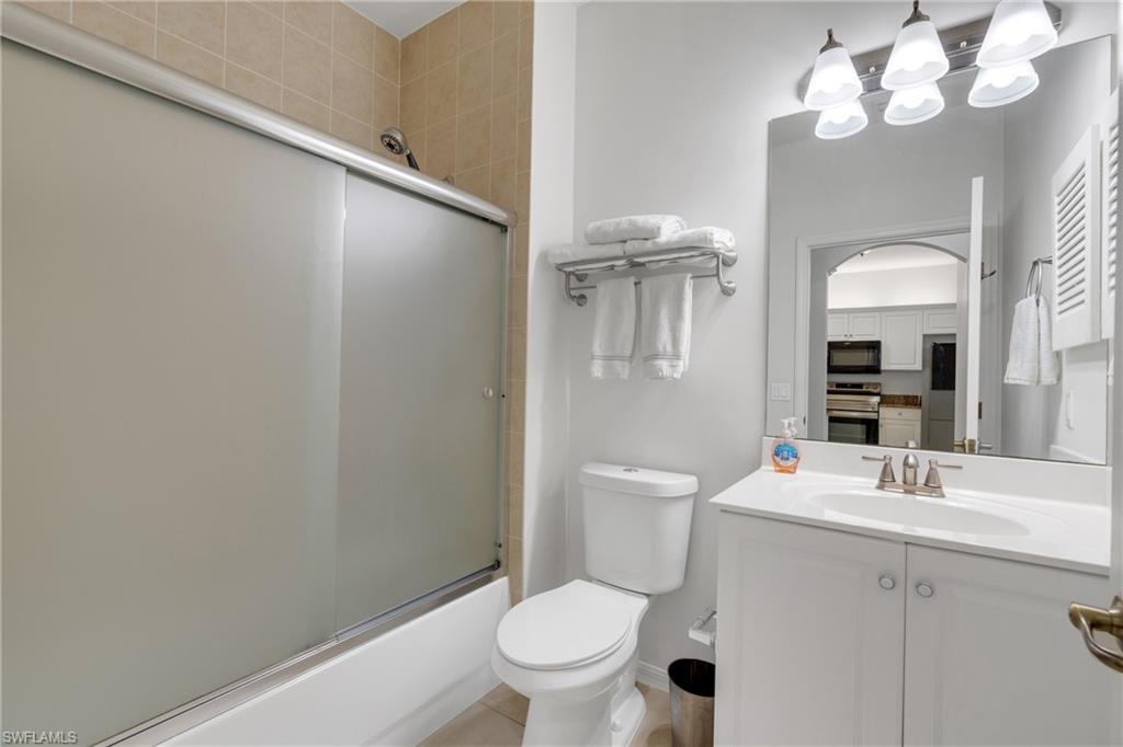 Bathroom featuring a white vanity with an integrated sink, brushed nickel faucet, a large wall-mounted mirror, and a shower-tub combination with a sliding frosted glass enclosure