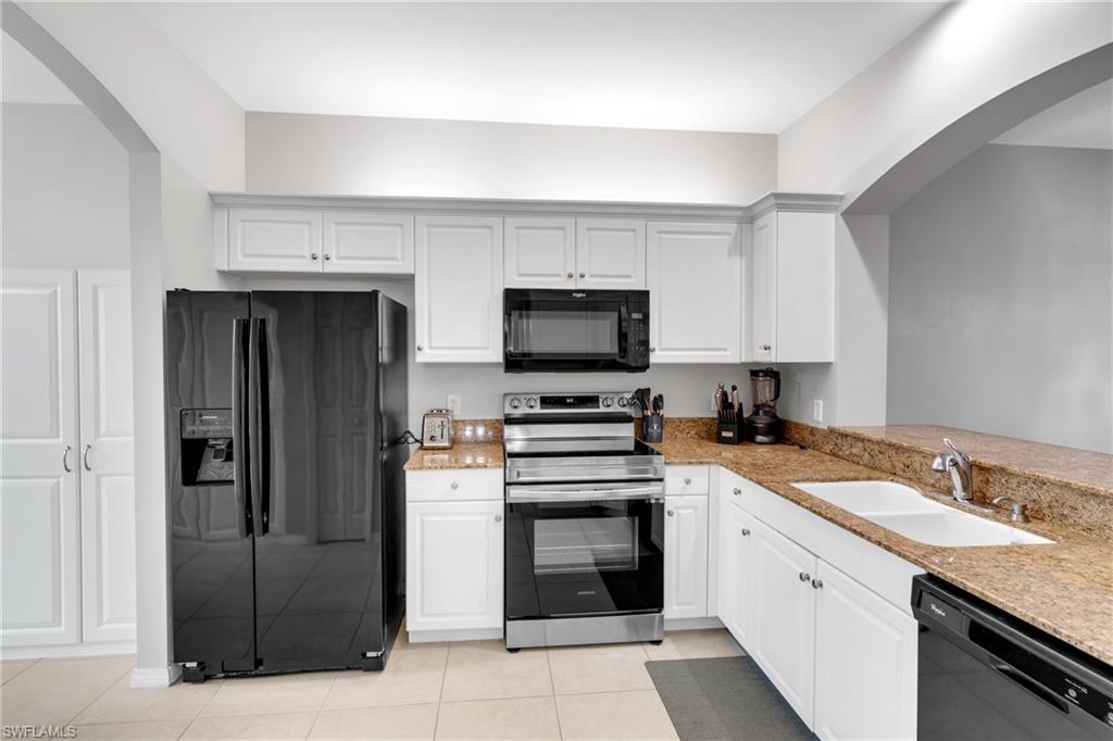 Kitchen featuring white cabinetry, black and stainless steel appliances, a double basin sink, and tile flooring