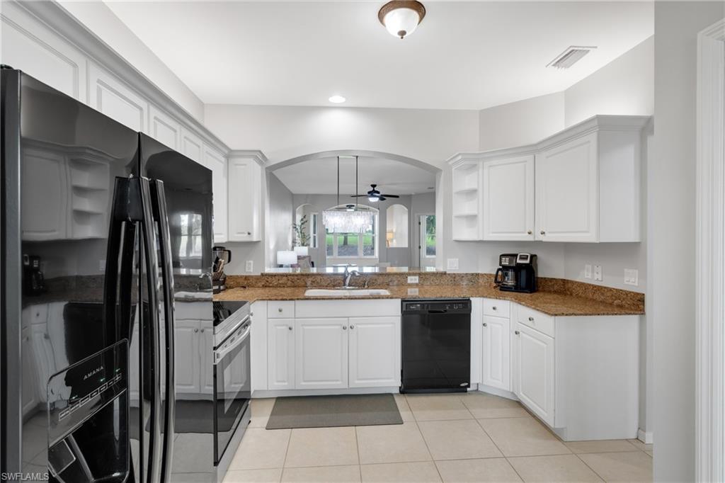 Chef's kitchen featuring white cabinetry, stainless steel appliances including double wall ovens and a black dishwasher, wood-finish countertops, ceramic tile flooring, and an arched passageway with transom windows overlooking the adjacent space