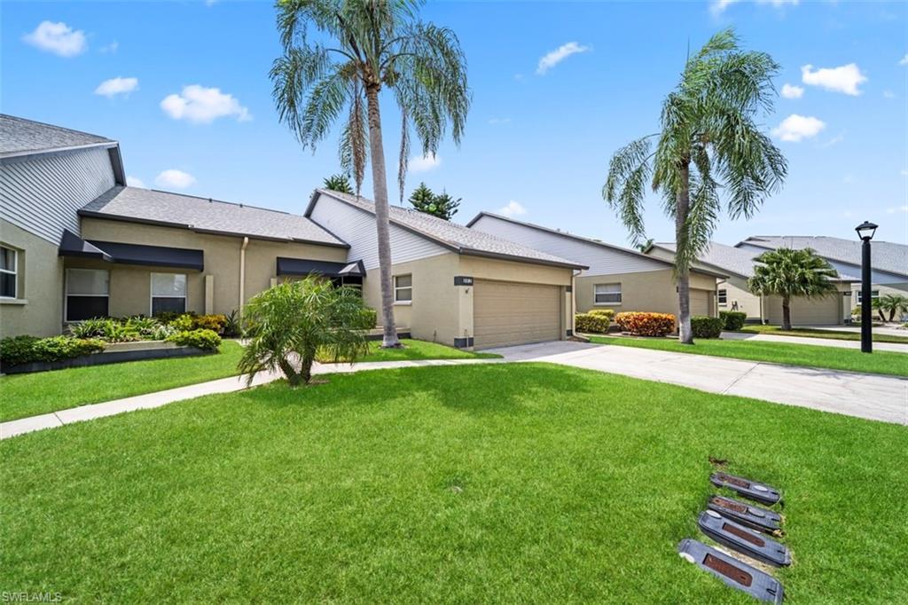Exterior featuring a covered entry, attached garage, well-maintained lawn, mature palm trees, and established landscaping