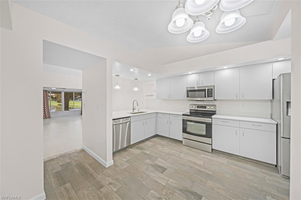 Kitchen featuring white shaker-style cabinetry, stainless steel appliances, light-colored countertops, and wood-look tile flooring
