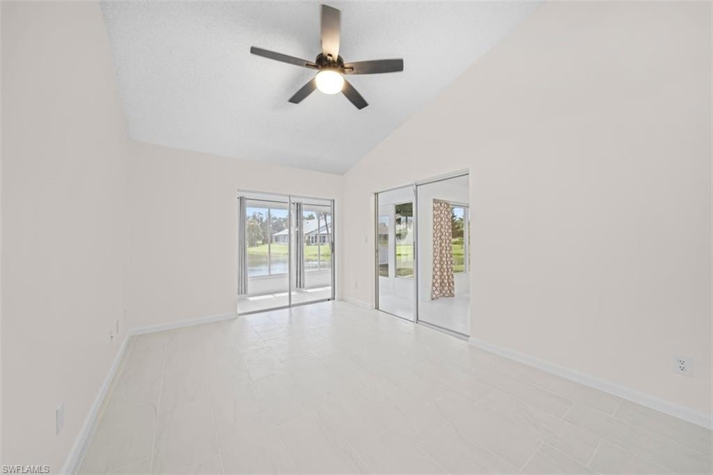 Vaulted ceiling with a ceiling fan, sliding glass doors, mirrored closet doors, and light-toned tile flooring