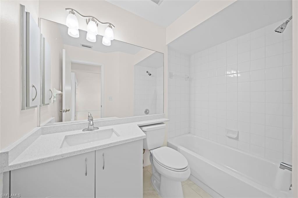 Bathroom featuring a vanity with an integrated sink, a large wall-mounted mirror, a built-in bathtub with white tile surround, and an overhead shower fixture