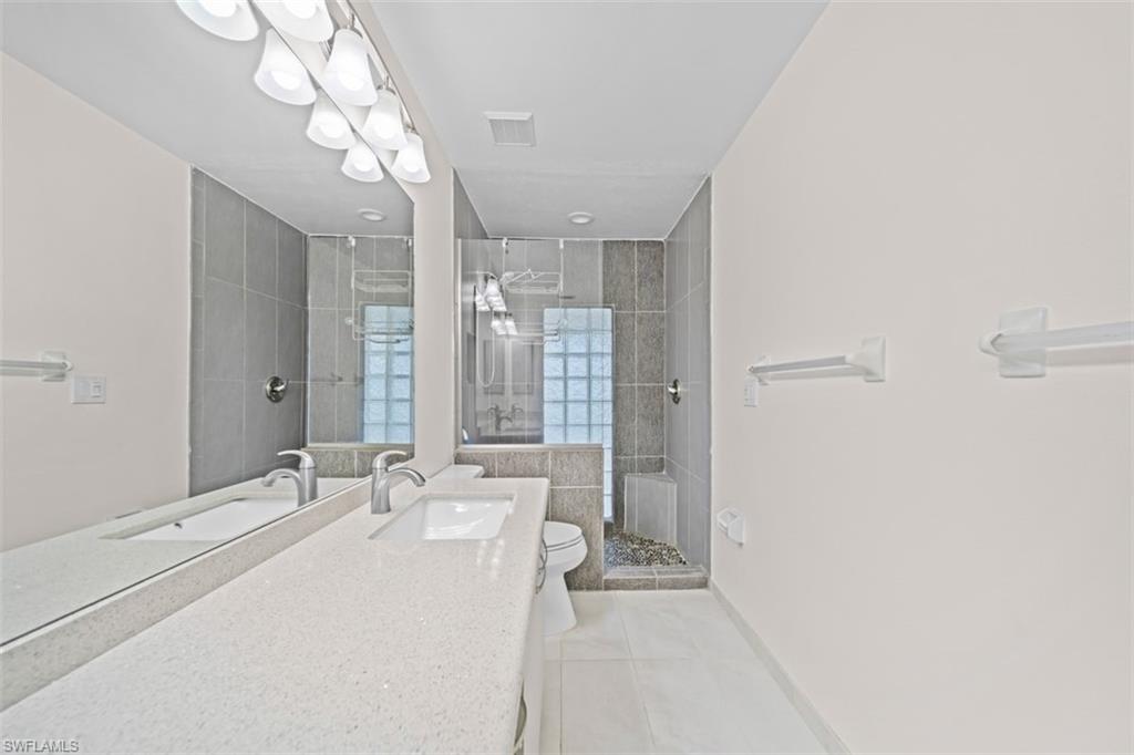 Double vanity with integrated sinks, extensive countertop space, large mirror, tile flooring, and a walk-in shower with glass block accents