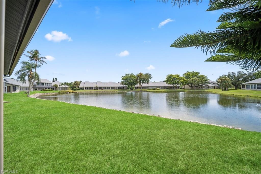 Expansive waterfront setting with lush green lawn, mature palm trees, and distant residential structures