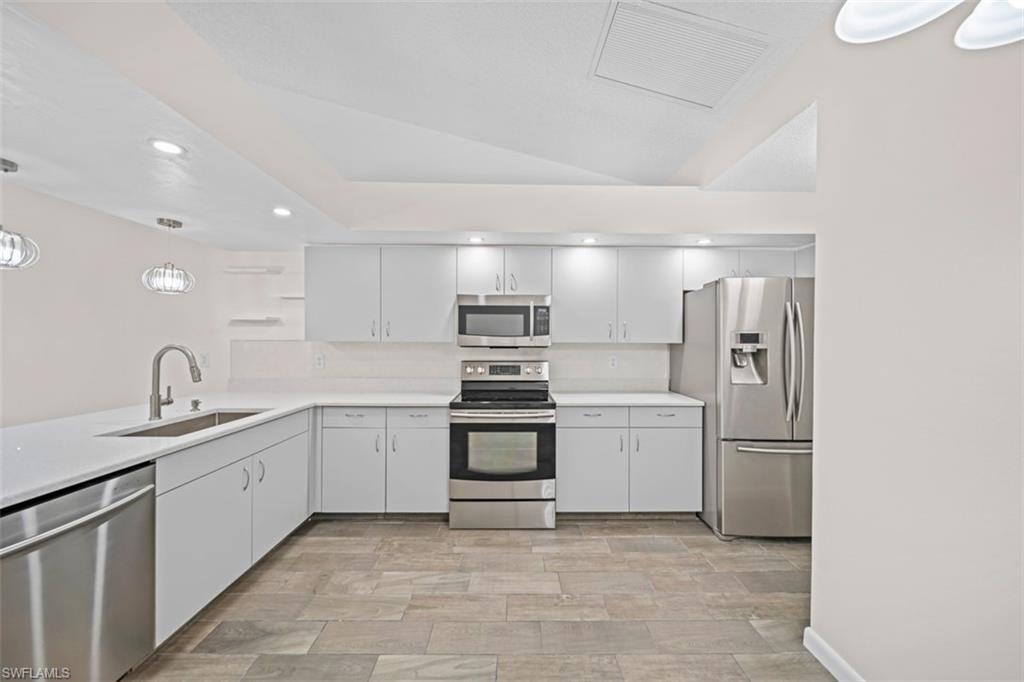 Modern kitchen featuring stainless steel appliances, white cabinetry, a large sink with a gooseneck faucet, and stone-look tile flooring