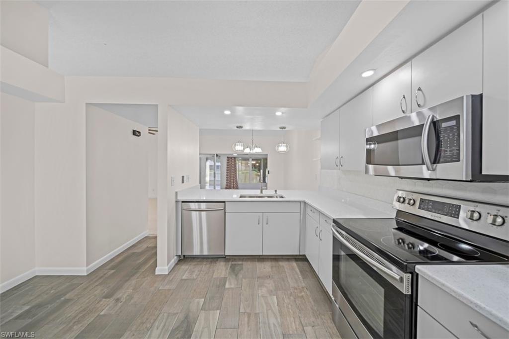 Modern kitchen featuring light cabinetry, stainless steel appliances, light countertops, a tile backsplash, and wood-finish flooring