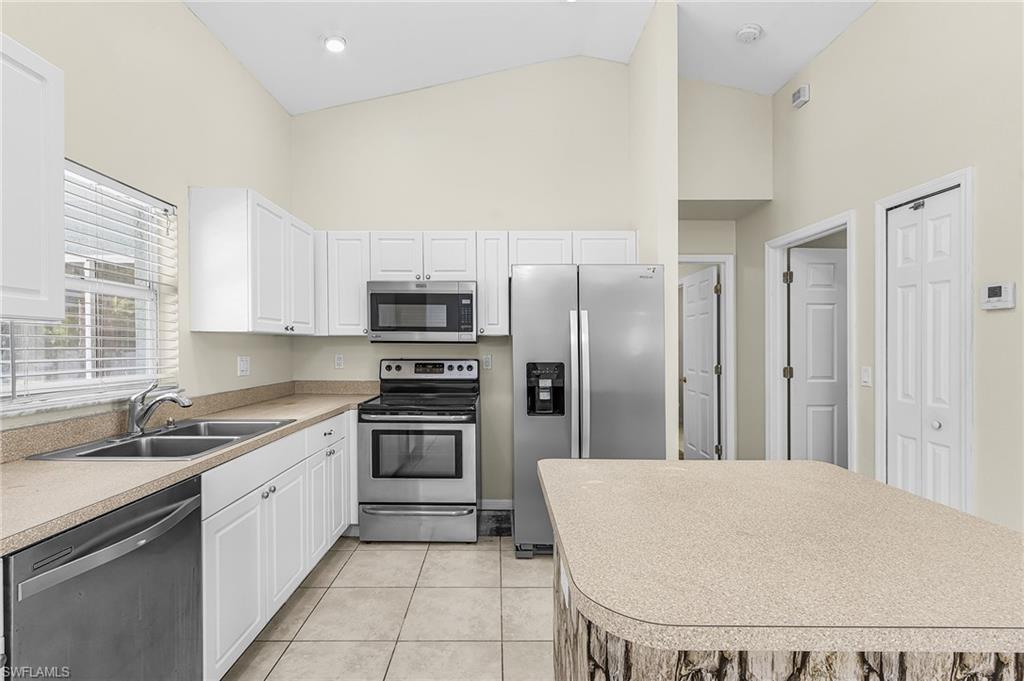 Vaulted ceilings, white cabinetry, stainless steel appliances, dual basin sink, and a kitchen island with a textured base