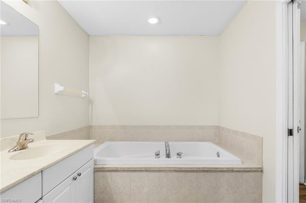 Built-in soaking tub with tile surround, vanity with an integrated sink, and recessed lighting
