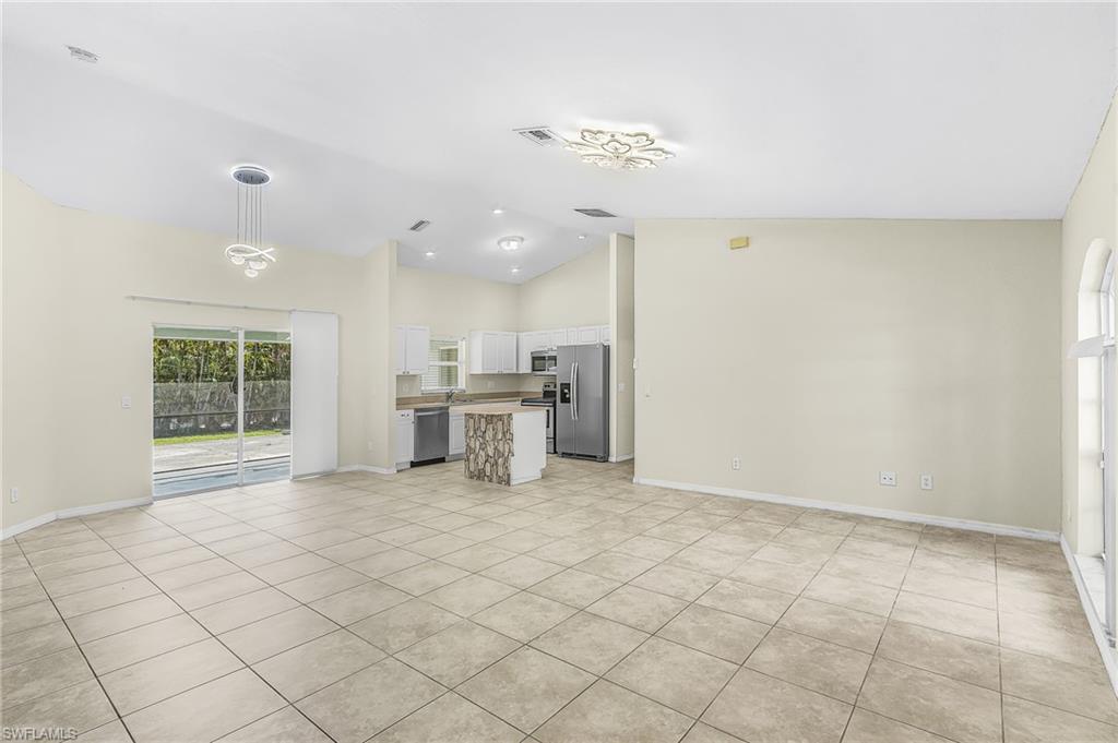Tile flooring, vaulted ceilings, sliding glass doors, white kitchen cabinetry, and stainless steel appliances