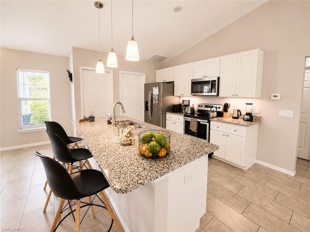 Vaulted ceiling kitchen featuring an extended island with a built-in sink, stainless steel appliances, white cabinetry, and tile flooring