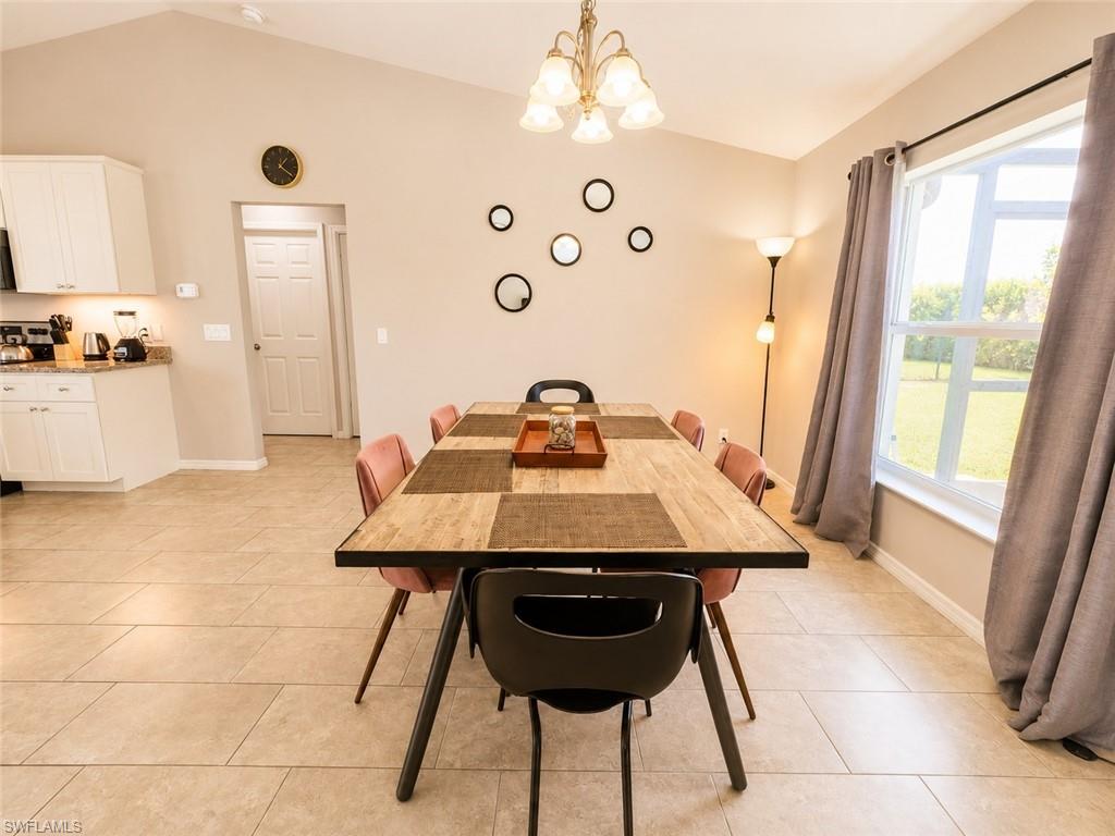 Vaulted ceiling, tile flooring, window with exterior scenery, kitchen cabinetry with granite-style countertop, and built-in ceiling light fixture