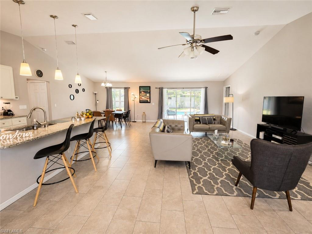 Open-concept living space with vaulted ceilings, large sliding glass doors, a kitchen island with seating, and tile flooring