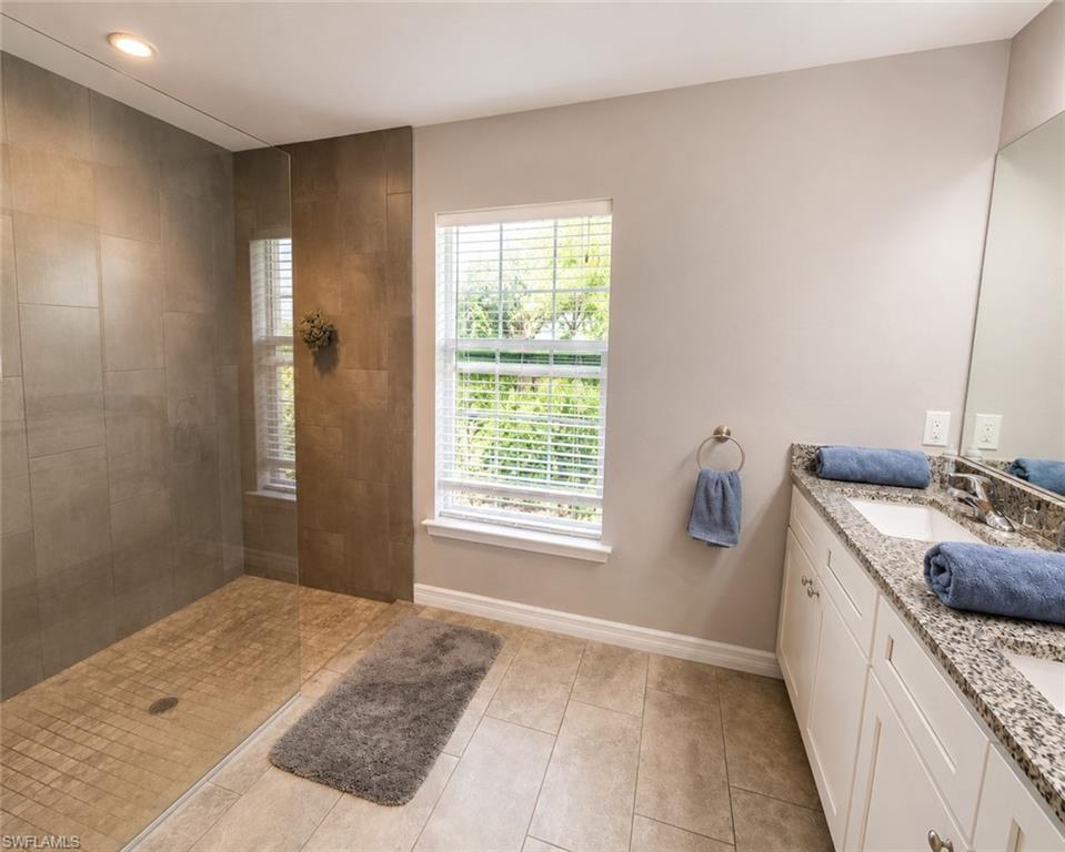 Spacious bathroom featuring a dual vanity with granite countertop, integrated sinks, white cabinetry, and a large mirror