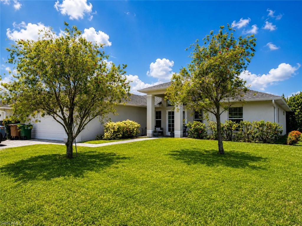 Well-manicured lawn with mature trees, a covered entry, and a two-car garage
