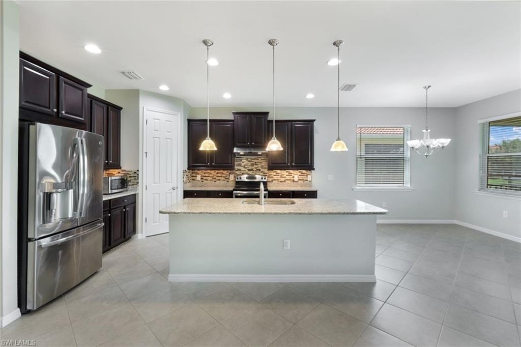 Kitchen featuring a center island with granite countertop, dark wood-finish cabinetry, stainless steel appliances, and a mosaic tile backsplash