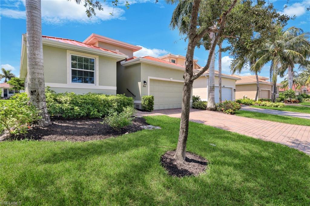 Single-story stucco exterior with a terra cotta tile roof, an integrated garage, a brick paver driveway, and established landscaping