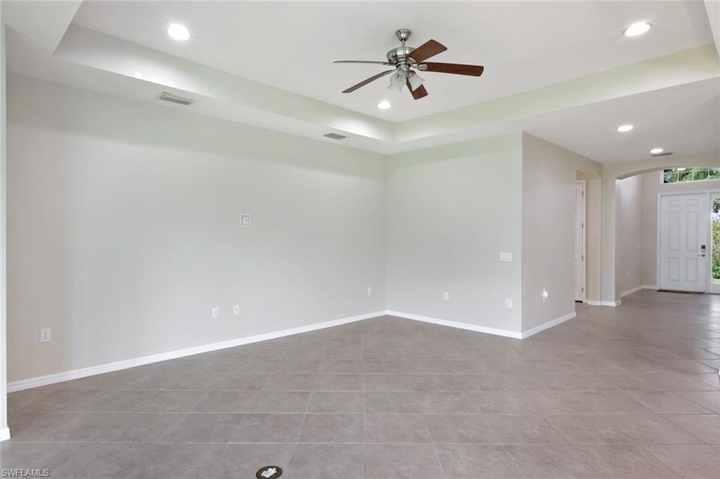 Tray ceiling with recessed lighting, ceiling fan, tile flooring, and a paneled entry door with transom window