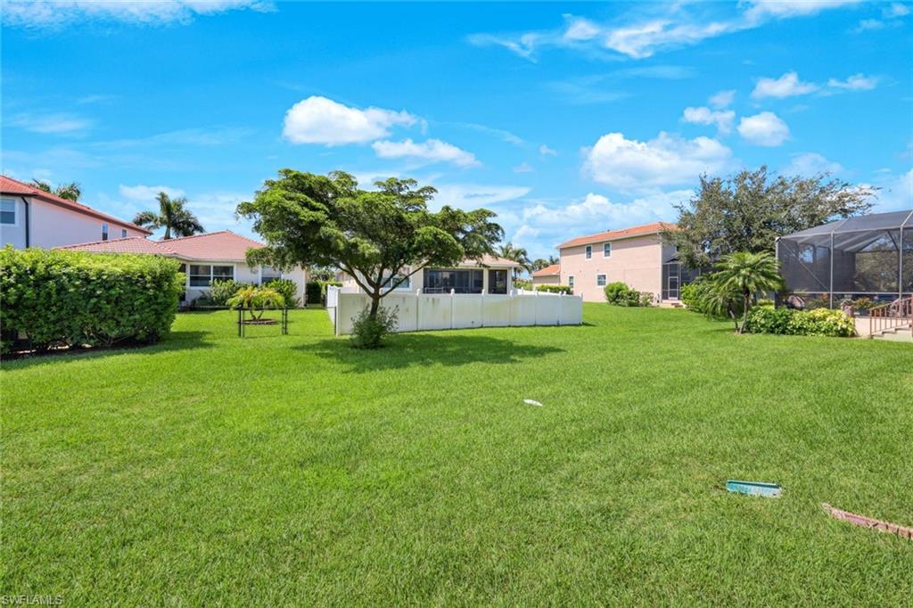 Expansive backyard featuring a manicured lawn, mature shade trees, and vinyl perimeter fencing
