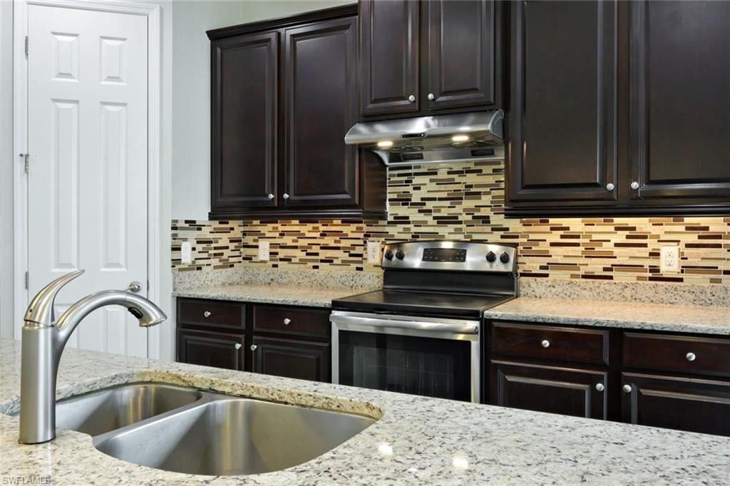 Granite countertops, dual basin sink with brushed nickel faucet, stainless steel range and hood, mosaic tile backsplash, and dark wood cabinetry