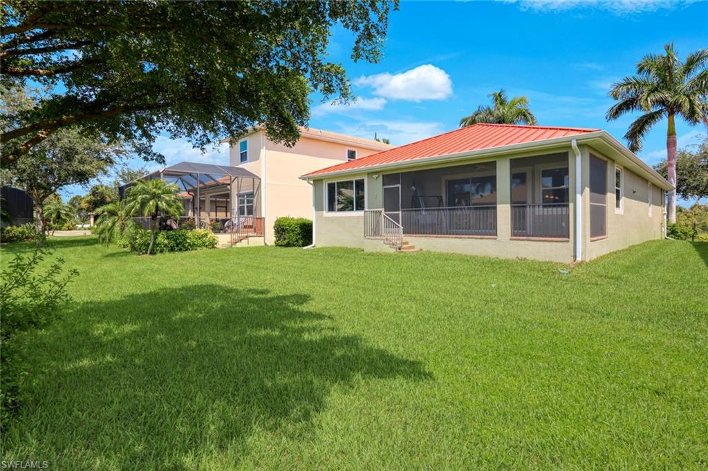 Expansive green lawn, screened-in porch with railing, red metal roof, mature palm trees, and established landscaping