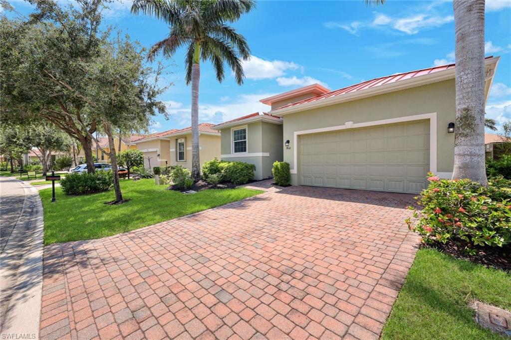 Paver driveway leading to an attached garage, mature landscaping, and a red tile roof
