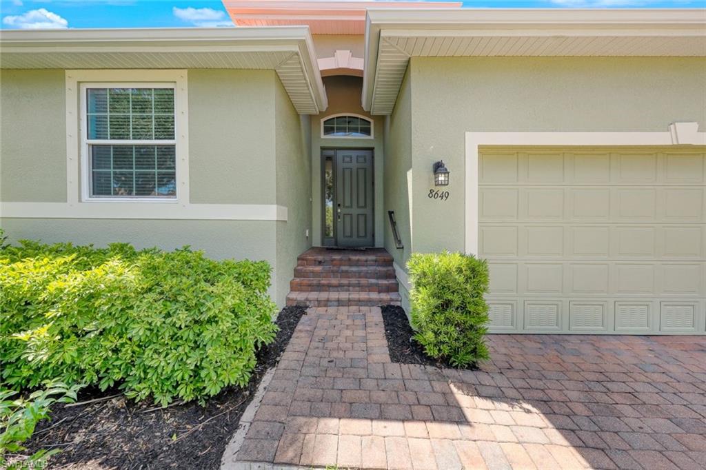 Exterior with stucco finish, paver driveway, mature landscaping, and a paneled garage door