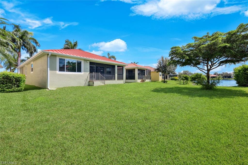 Expansive backyard featuring a manicured lawn, screened patio, and mature trees overlooking a body of water