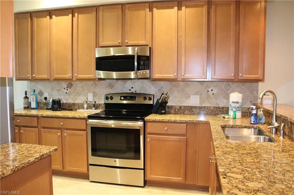 Kitchen with appliances with stainless steel finishes, light stone counters, brown cabinetry, and decorative backsplash