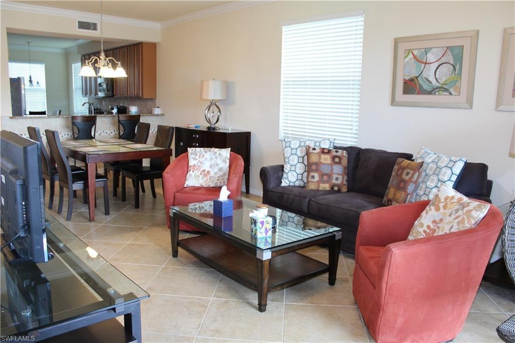 Living room with light tile patterned floors, ornamental molding, and a chandelier
