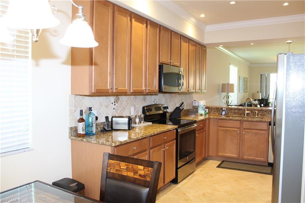 Kitchen featuring brown cabinets, decorative light fixtures, stainless steel appliances, dark stone counters, and ornamental molding